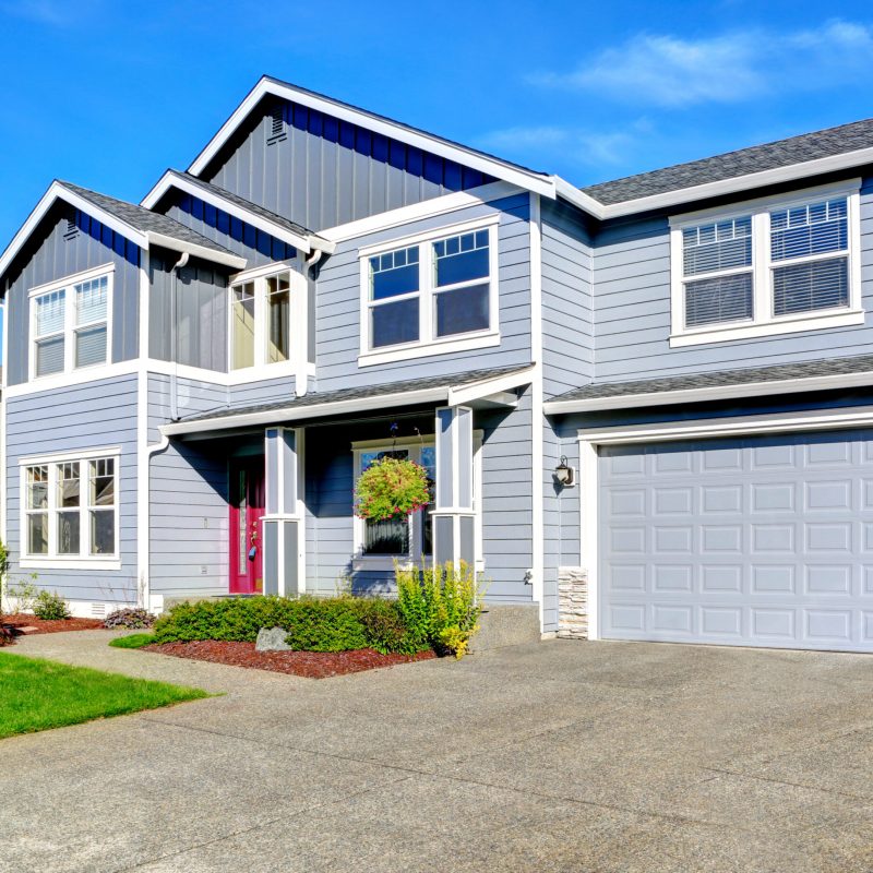 Light blue two story house with column entrance porch, garage and driveway view